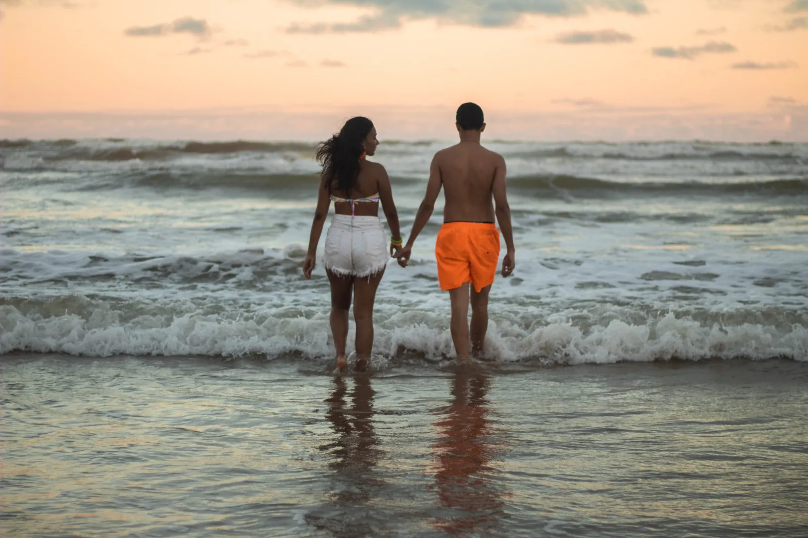 A couple holding hands as they walk into the sea at sunset